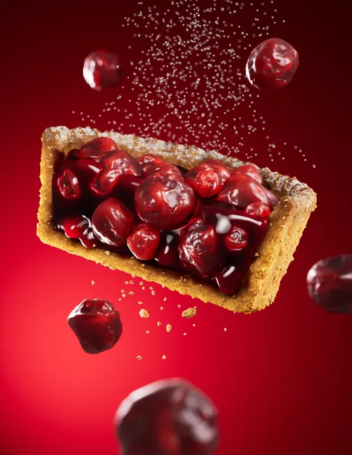 Tarte aux cerises avec des cerises flottantes et des miettes sur fond rouge, par Dan Couto