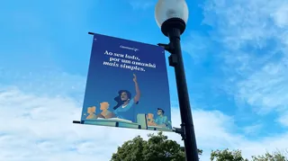 Street banner with text in Portuguese and cartoon people under blue sky