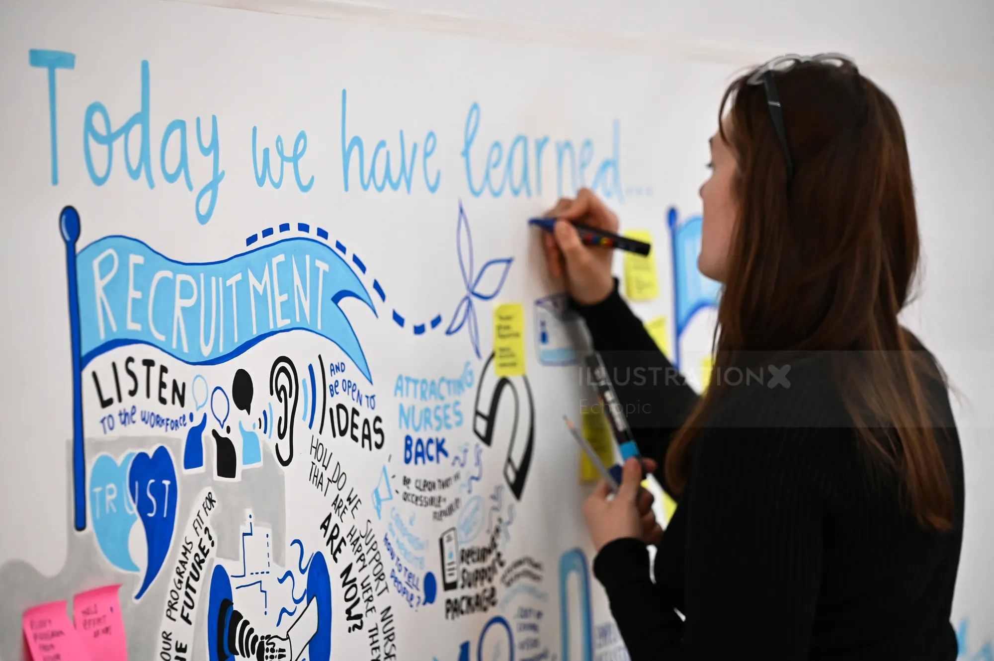 Woman writing recruitment ideas on whiteboard with colorful markers.