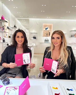 Two women seated indoors holding Dior booklets by Elise Lee