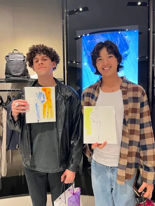 Two men holding fashion sketches at Emporio Armani event by Elise Lee