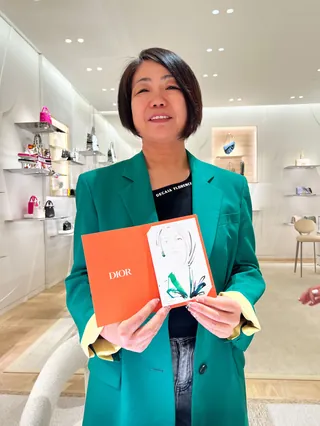 Woman in green blazer holding open Dior booklet, by Elise Lee Live Event Drawing