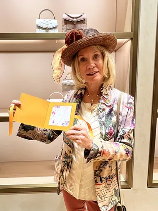 Woman in floral jacket and hat holding a yellow card inside a luxury store