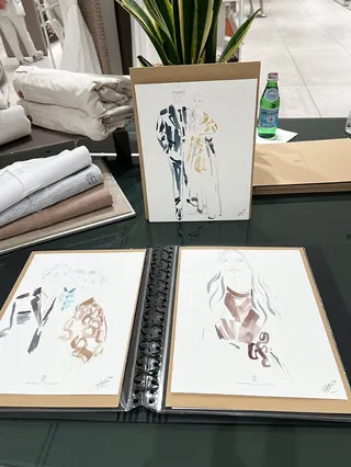 Fashion sketches in a binder and framed on a table with fabric samples