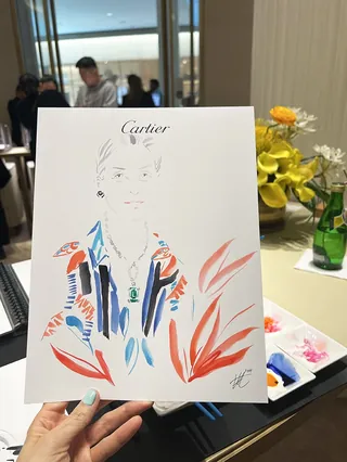 Hand holding a Cartier event sketch of a woman with colorful clothing