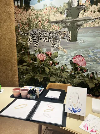 Sketches and paint pots in front of a leopard mural with flowers