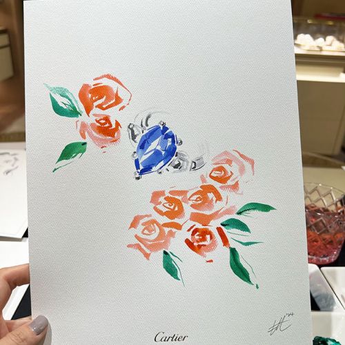 Hand holding artwork with blue gemstone and orange flowers