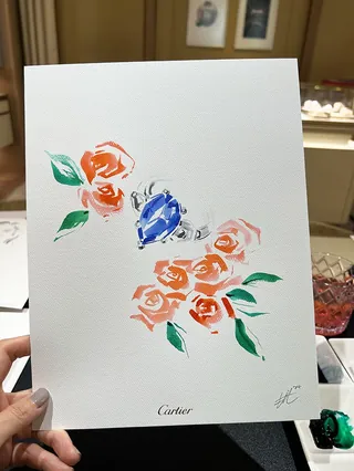 Hand holding artwork with blue gemstone and orange flowers