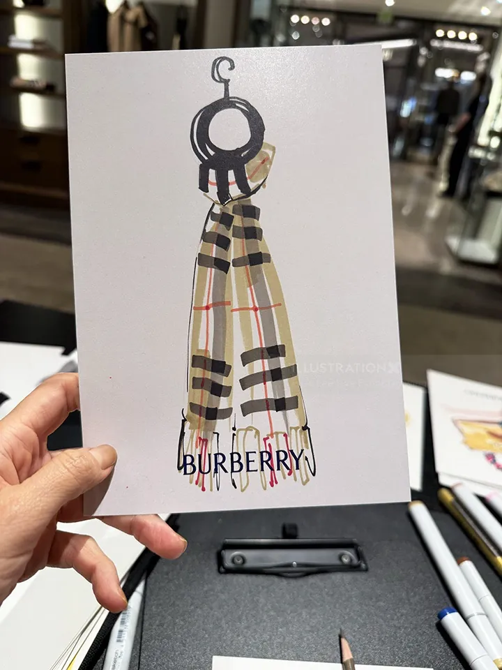Hand holding a live sketch of a Burberry scarf by Elise Lee