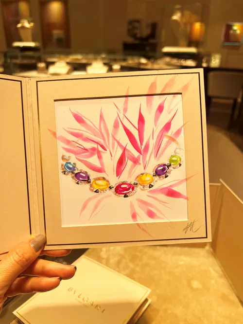 Hand holding BVLGARI jewelry illustration with colorful gems by Elise Lee