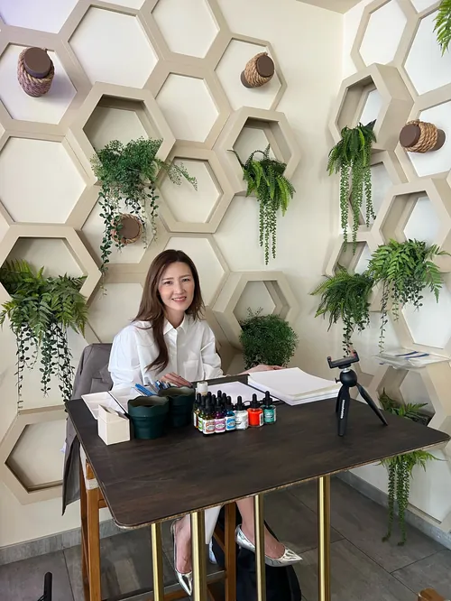Woman sitting at table with art supplies and hexagonal plant wall by Elise Lee