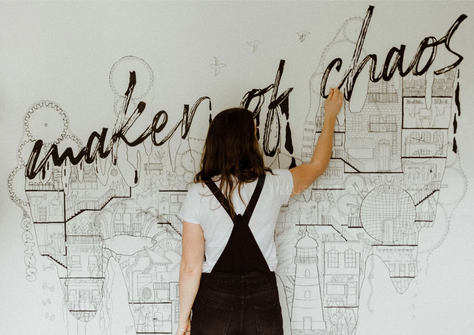 Woman writing the phrase maker of chaos on wall artwork by Ellie Compton