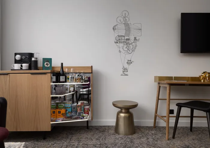 Hotel room with bar cart, metallic stool, and wall art by Ellie Compton