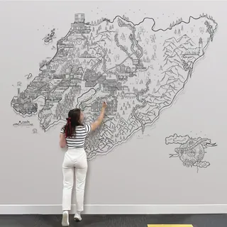 Woman drawing intricate fantasy map on white wall with black ink