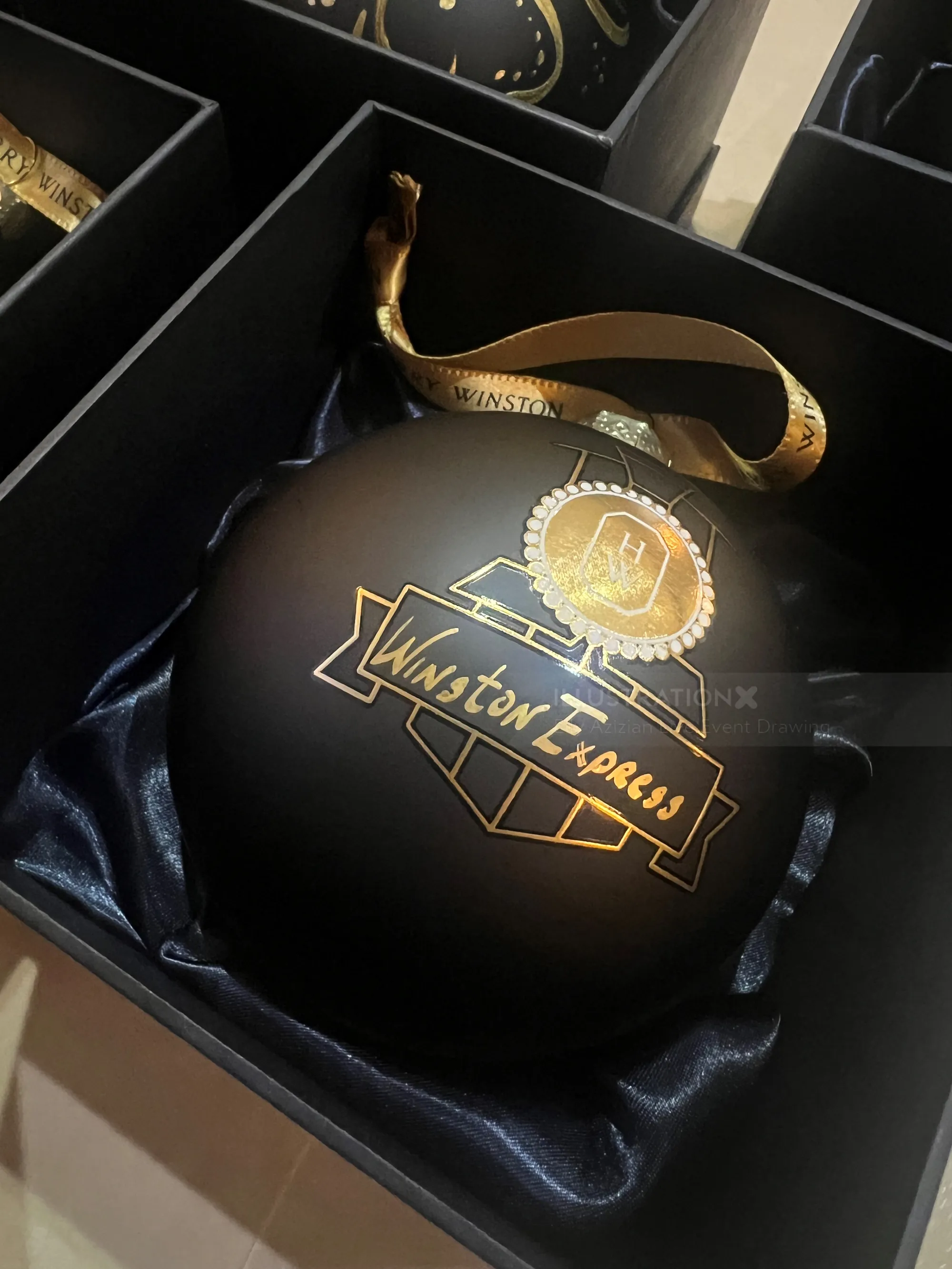 Adorno navideño negro con logotipo y cinta de Winston Express dorados.