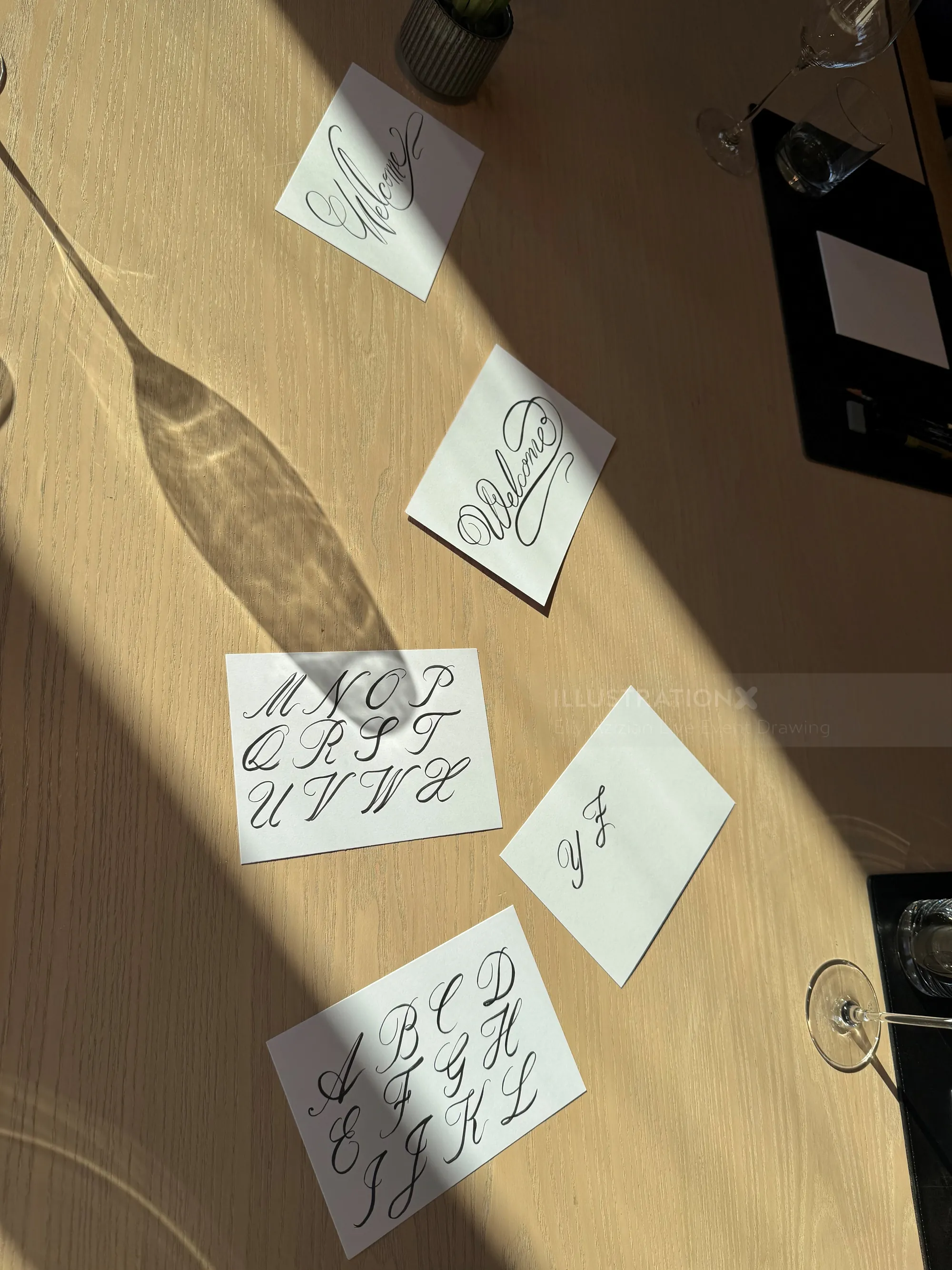 Calligraphy practice sheets showing cursive alphabet letters on a wooden table