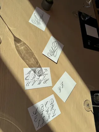 Calligraphy practice sheets showing cursive alphabet letters on a wooden table