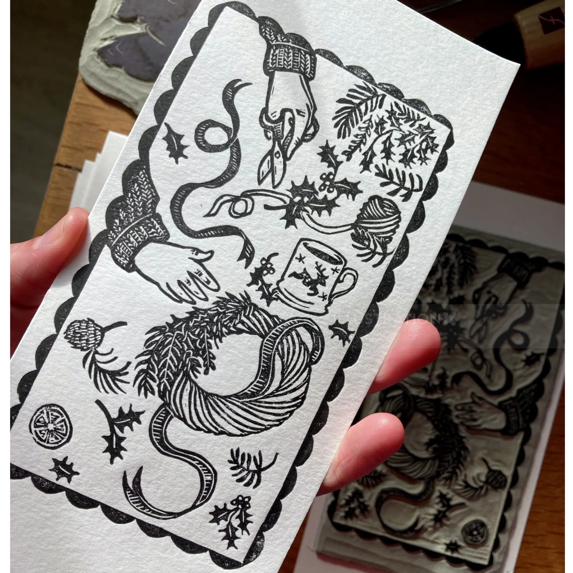 Black and white lino cut showing hands making a Christmas wreath, by Emily Robertson