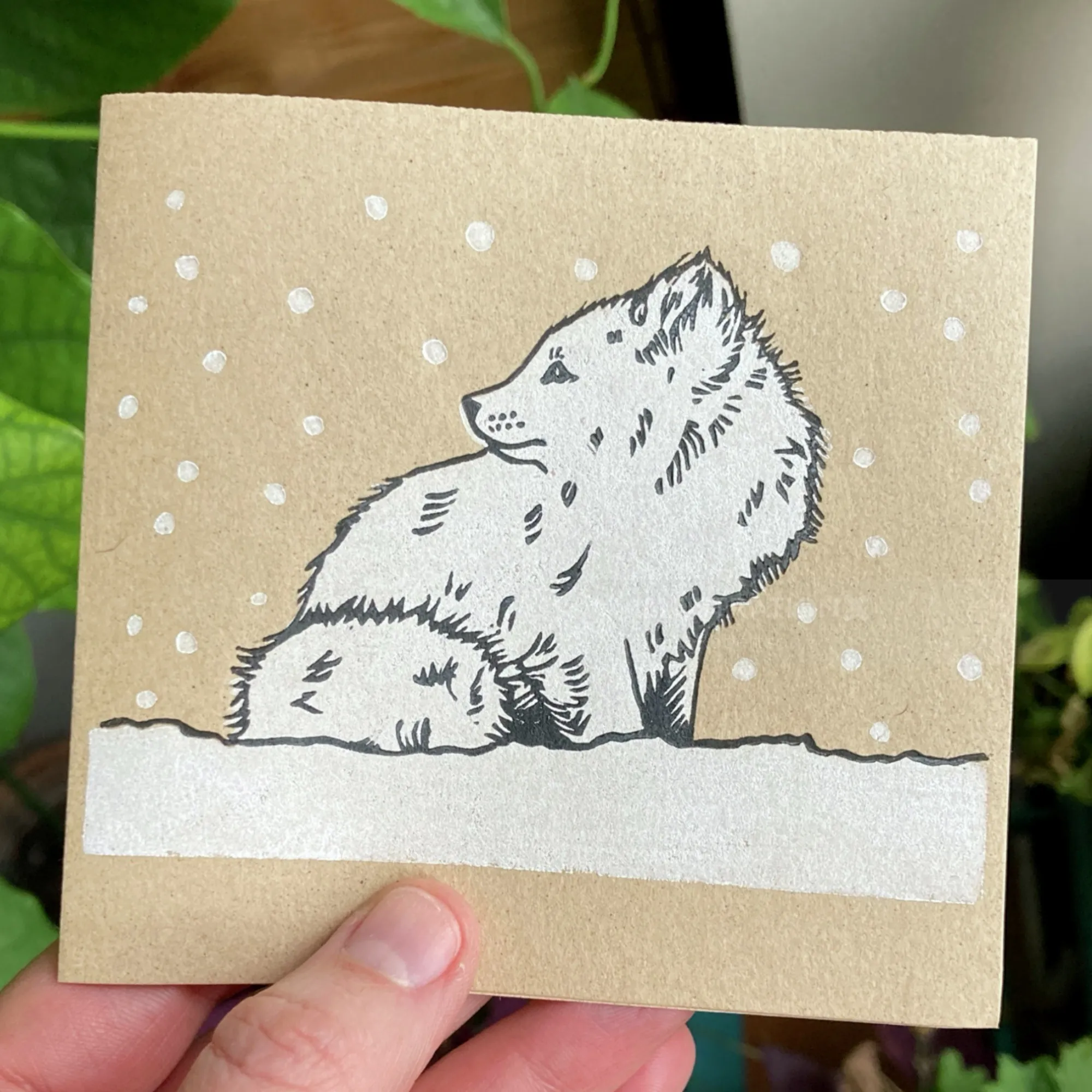 Lino cut of an arctic fox sitting in snow by Emily Robertson