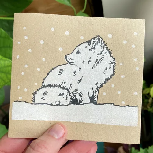 Lino cut of an arctic fox sitting in snow by Emily Robertson