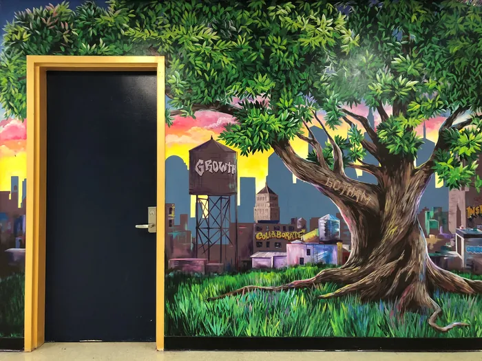 Mural showing a large tree and city skyline with a black door by Esther Stimphat