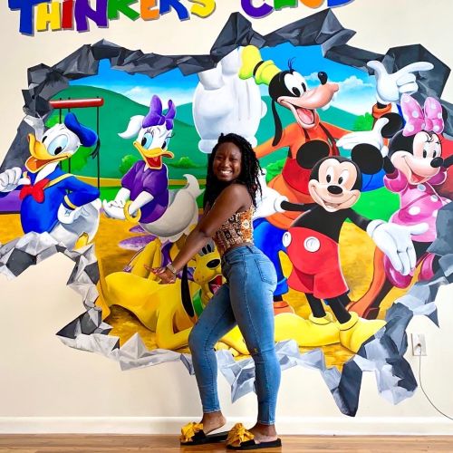 Woman posing by Disney characters mural on wall by Esther Stimphat