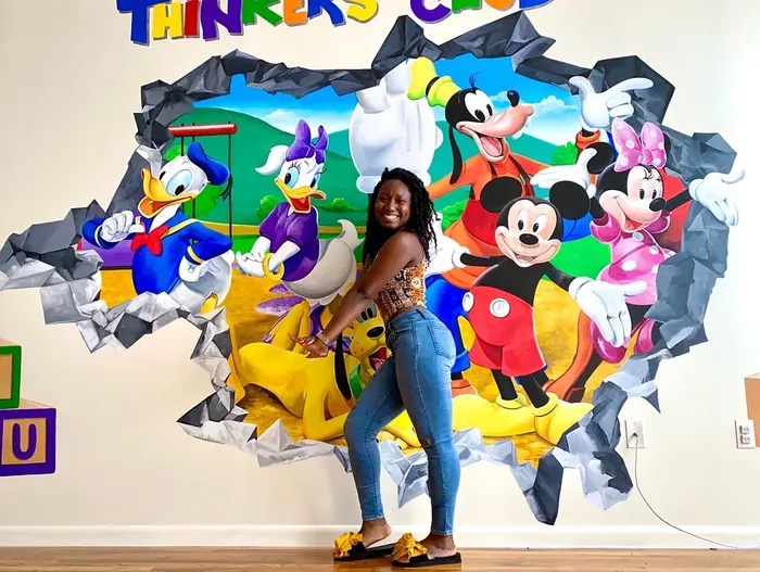 Woman posing by Disney characters mural on wall by Esther Stimphat
