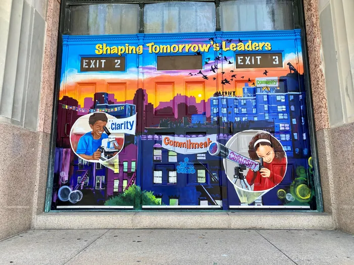 Mural showing cityscape and children learning, by Esther Stimphat