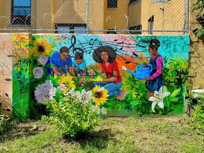 Mural of people gardening with sunflowers and musical notes on brick wall