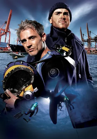 Two divers wearing wetsuits and underwater equipment near harbor cranes by Frank Neidhardt
