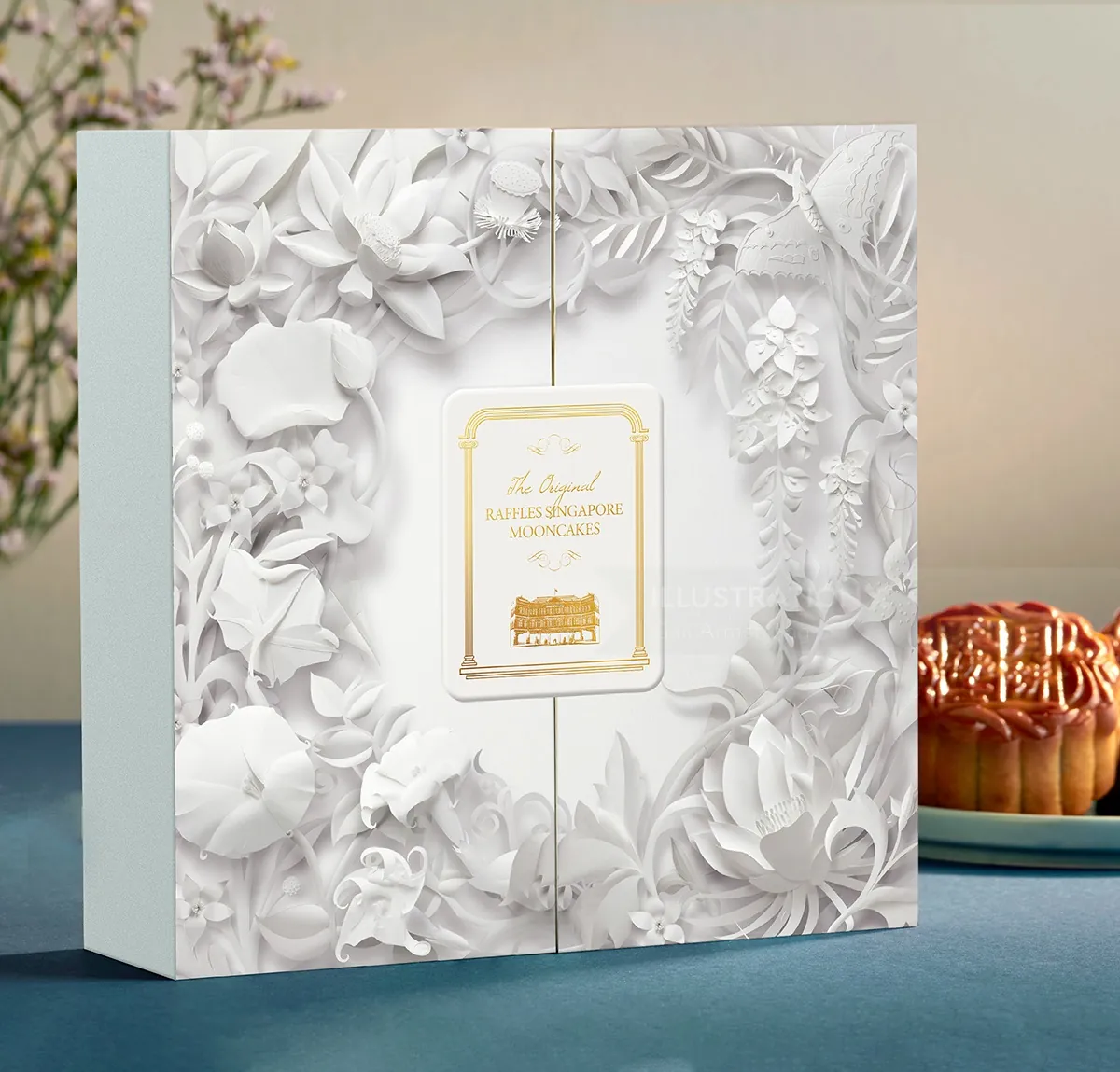 Weiße, blumengeprägte Verpackungsbox mit goldenem Etikett auf blauem Grund