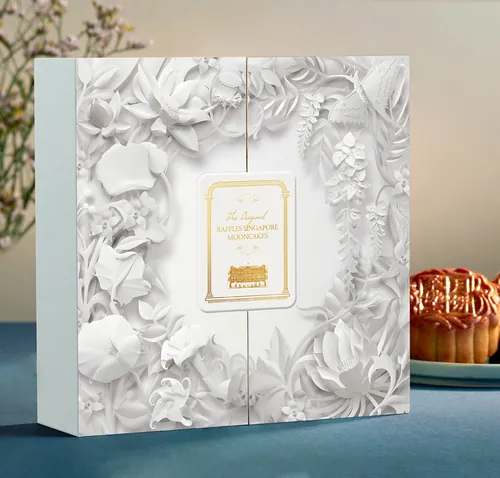 Weiße, blumengeprägte Verpackungsbox mit goldenem Etikett auf blauem Grund