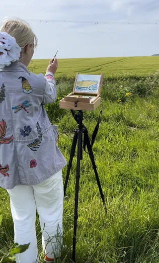 Georgie Stewart painting a green field landscape on easel outdoors