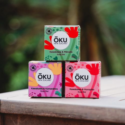 Three stacked Oku soap bars with colorful packaging outdoors