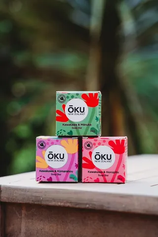 Three stacked Oku soap bars with colorful packaging outdoors