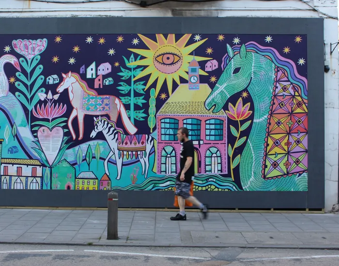 Colorful mural depicting horses, a house, and a sun by Hannah Davies