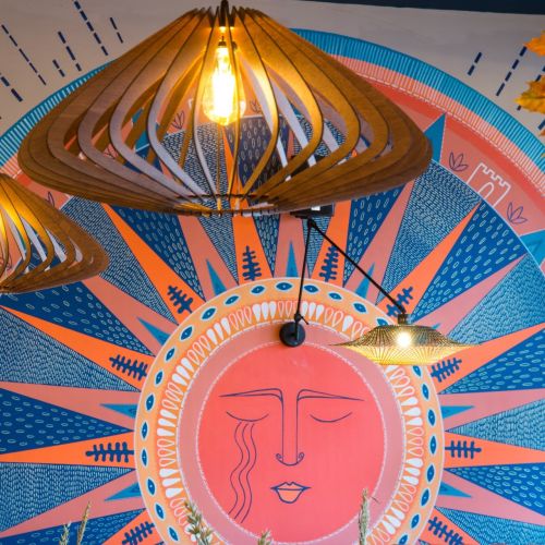 Colorful mural with a sun face and hanging wooden light fixtures
