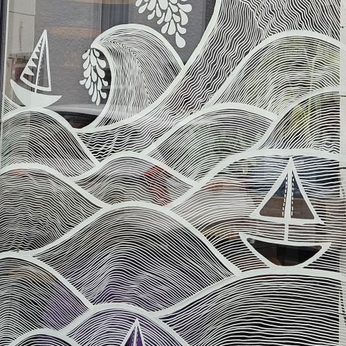 White line art mural of waves, birds and sailboats on window