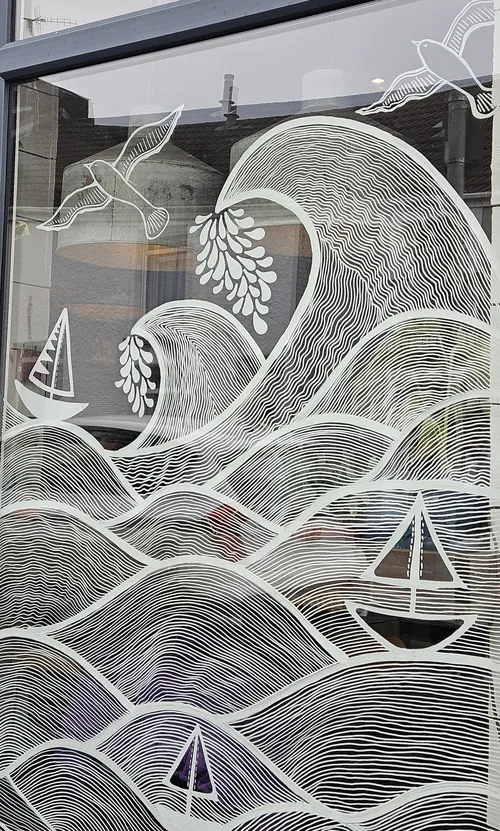 White line art mural of waves, birds and sailboats on window
