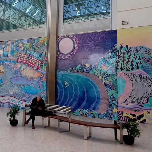 Mural with ocean waves and wildlife, woman sitting on bench below