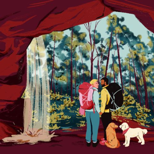 Dos excursionistas con mochilas y perros dentro de una cueva cerca de una cascada.