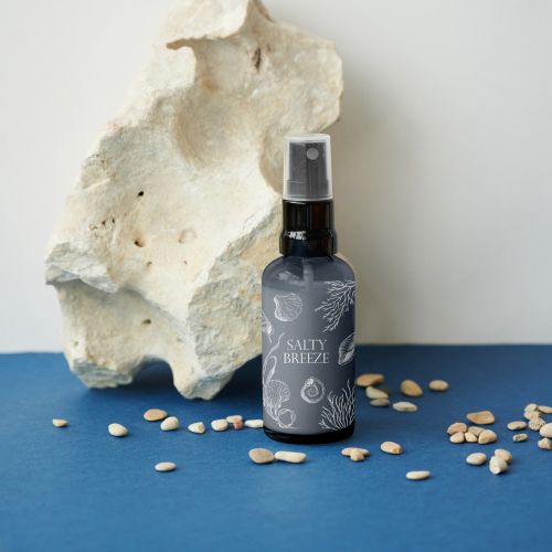 Dark spray bottle labeled salty breeze with white stone and scattered seeds on blue surface