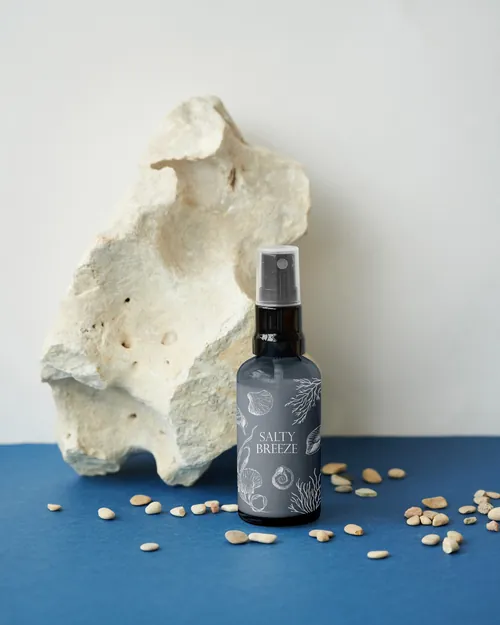 Dark spray bottle labeled salty breeze with white stone and scattered seeds on blue surface