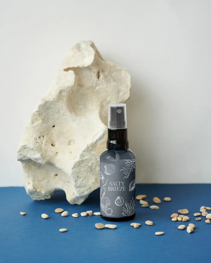 Dark spray bottle labeled salty breeze with white stone and scattered seeds on blue surface