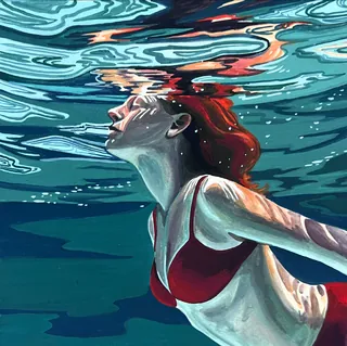 Woman with red hair swimming underwater in red swimsuit