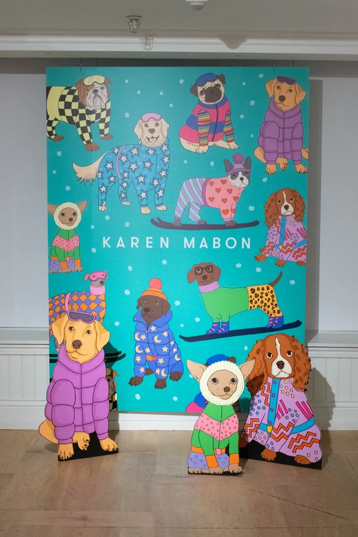 Cartoon dogs wearing colorful winter clothes in front of Karen Mabon poster