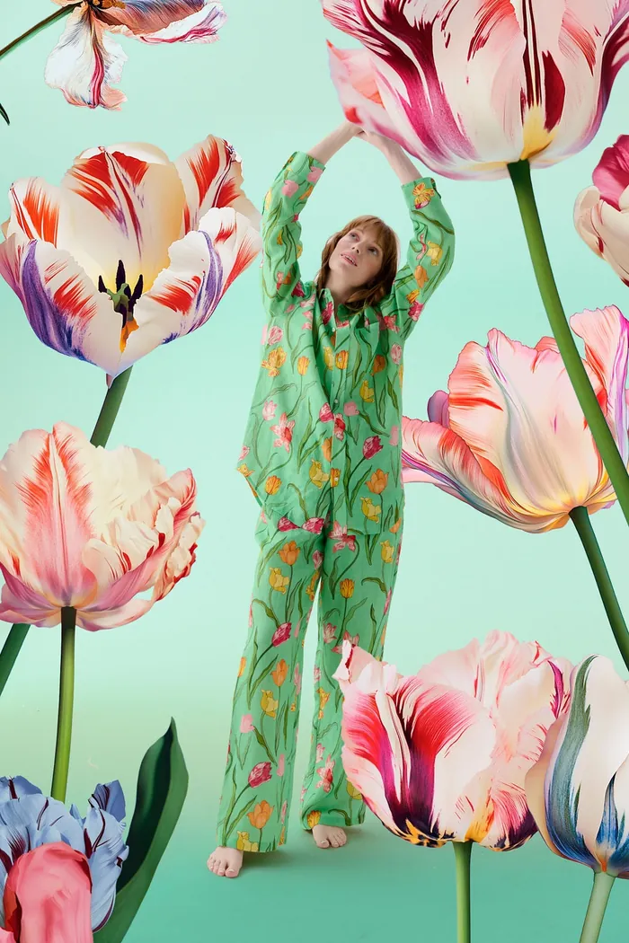 Person in green floral pajamas standing among large pink and purple tulips