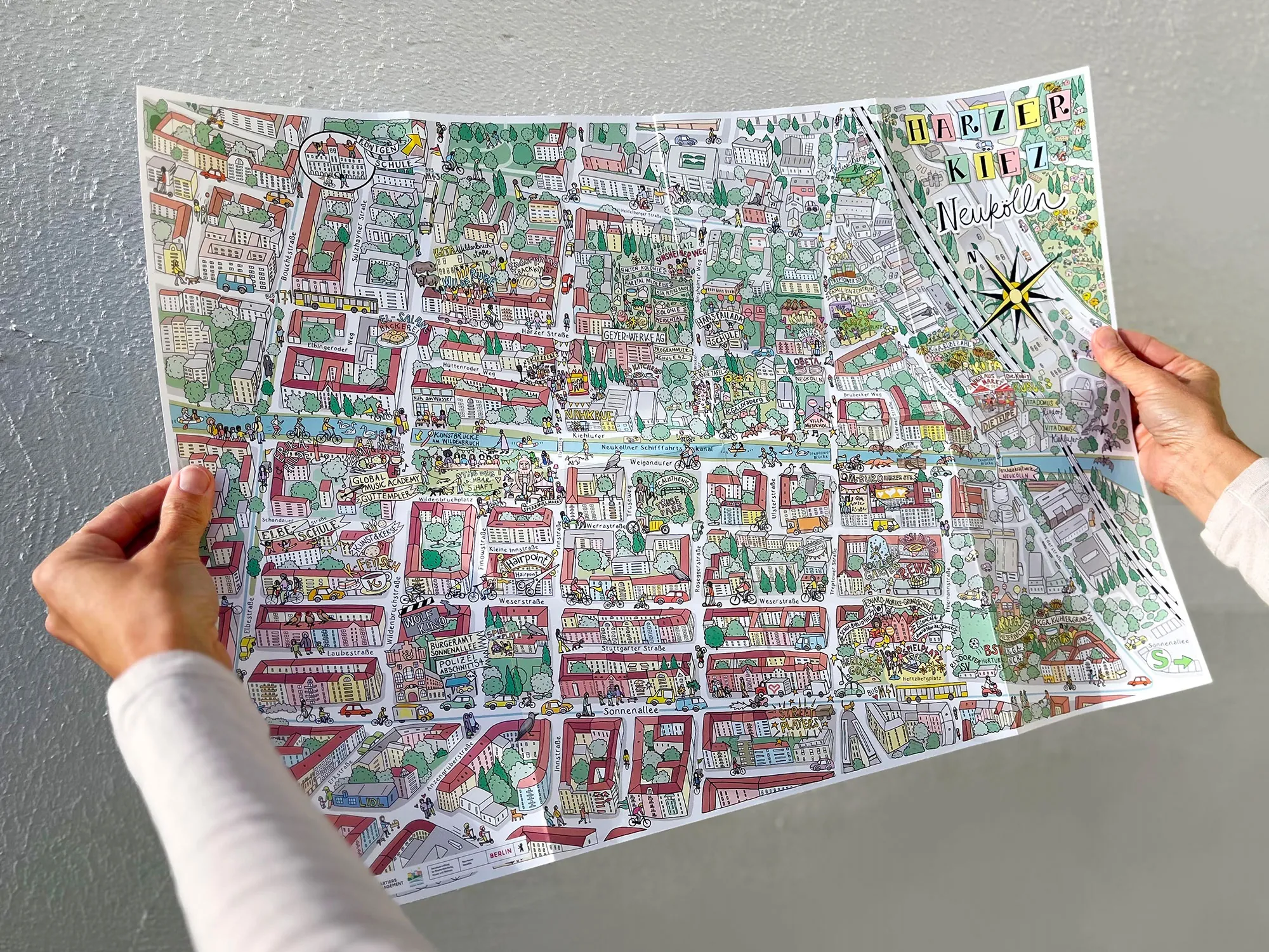 Carte de ville illustrée et colorée tenue par deux personnes, œuvre de Katherine Kannon