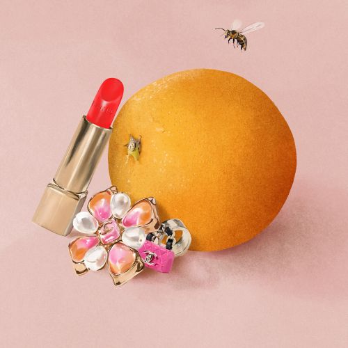 Red lipstick, orange, flower brooch, and bee on pink background