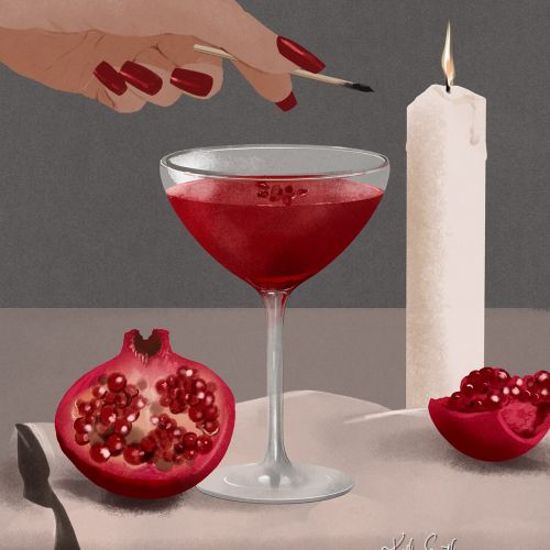 Hand with red nails and cocktail glass with pomegranate and candle